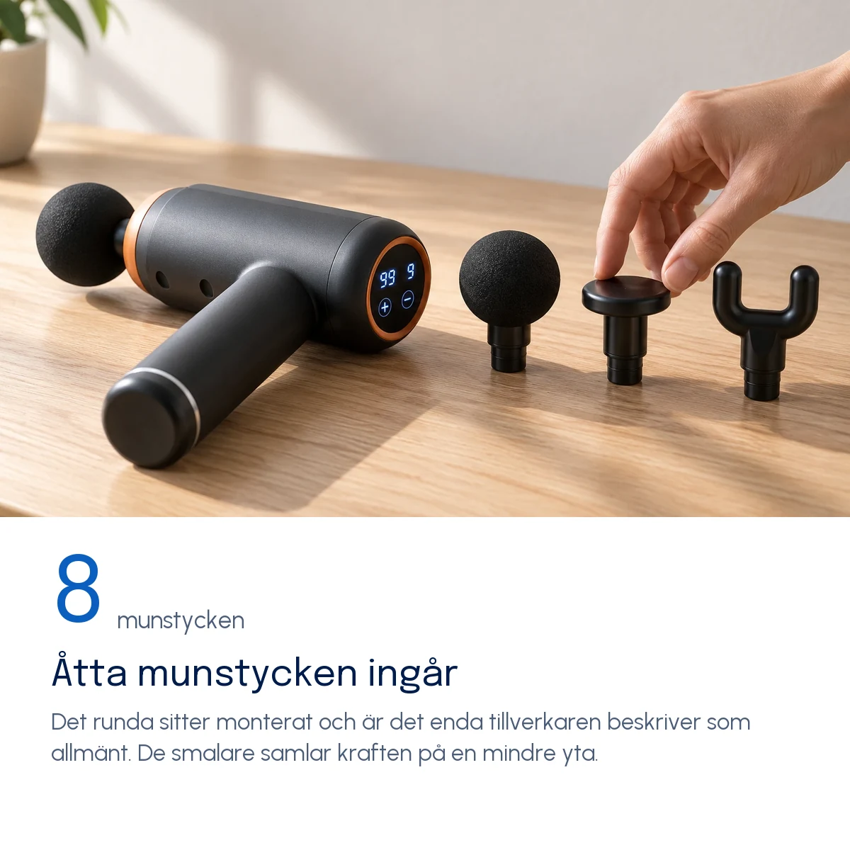 Åtta munstycken ingår — Massagepistolen på ett träbord med det runda munstycket monterat och tre lösa munstycken bredvid